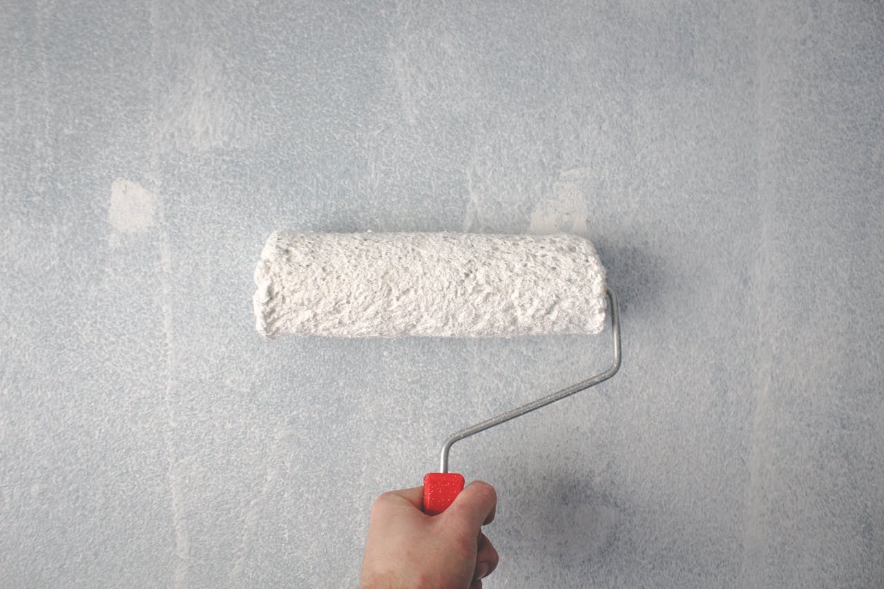 brand-01 A person's hand using a paint roller to apply white paint on a wall.
