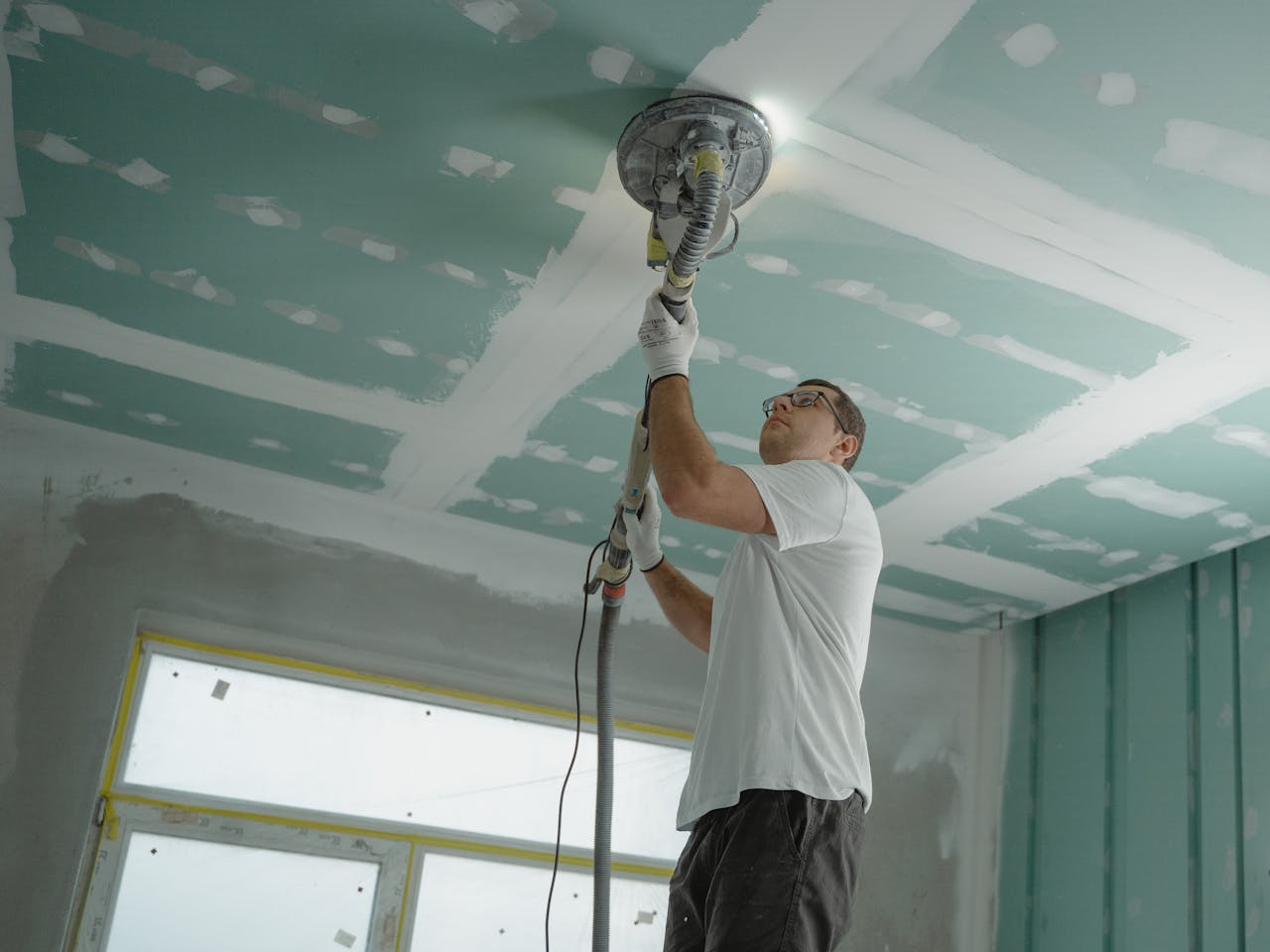 brand-02 A professional worker sanding the ceiling during a home renovation project. Indoor construction setting.